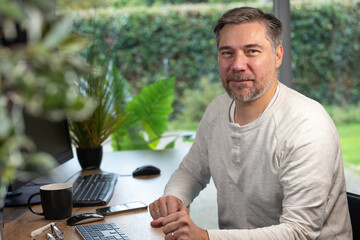 portrait d'un employé de bureau ou d'un homme d'affaires qui est assis à son bureau devant son ordinateur il est souriant et sympathique. Il est heureux de travailler chez lui à distance