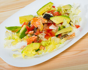 Healthy salad with chopped fried salmon, avocado, fresh tomatoes and Chinese cabbage on white plate
