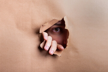 Man eye looking through a hole in a sheet of paper.
