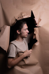 A man peering through a hole in a sheet of brown paper. Tearing the paper with his hands.