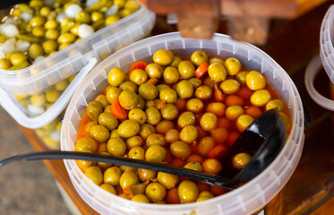 Pile of large green pitted olives lies in bucket with carrots and garlic in greengrocer's shop..