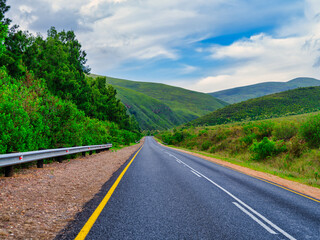 Road winding through rolling hills and mountains under blue sky with white clouds, Suurbraak, Western Cape, South Africa