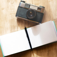 A retro film camera and a notepad with a pen lie on a wooden table, under the rays of the morning sun