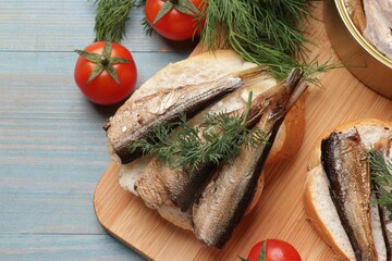 Delicious sandwiches with sprats, dill and tomatoes on light blue wooden table, top view
