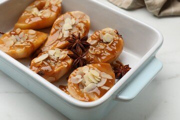Delicious pears with caramel sauce, almond flakes and anise stars in baking dish on white marble table, closeup
