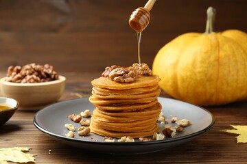 Pouring honey onto tasty pumpkin pancakes with walnuts at wooden table, closeup