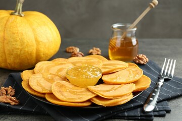 Tasty pumpkin pancakes with honey, walnuts and jam on grey table, closeup