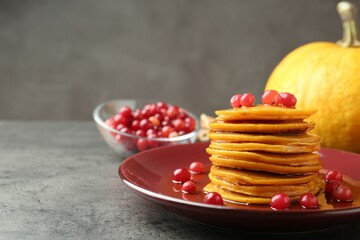 Tasty pumpkin pancakes with cranberries and honey on grey table, closeup. Space for text