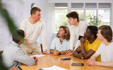 Concentrated team leader giving instructions to group of men, executives or employees during informal work meeting at table in office