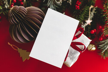 Christmas card mock up. Empty greeting card flat lay with fir branches, golden ornaments and gift on red background. Merry Christmas. Season greeting postcard template