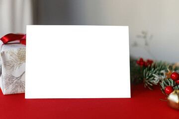 Empty greeting card and fir branches, red berries, gold ornaments on red background. Christmas card mockup with space for text.  Xmas Postcard. Season greetings card template