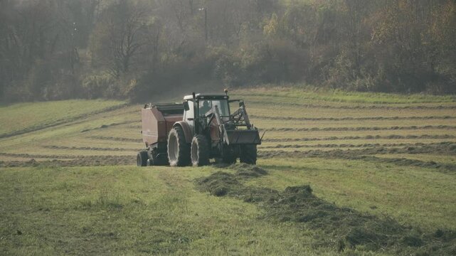 Modern tractor with hay baler or hay maker collects cut grass in the field. France