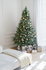 Wrapped holiday gift boxes under beautifully decorated Christmas tree with gold ornaments on white wooden wall panels background. Joyful atmosphere of winter holidays. Wallpaper, background, backdrop