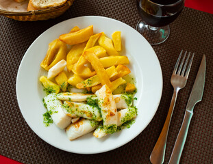 large piece of fried cuttlefish drizzled with white garlic and parsley sauce,lemon wedge and french fries on white plate.