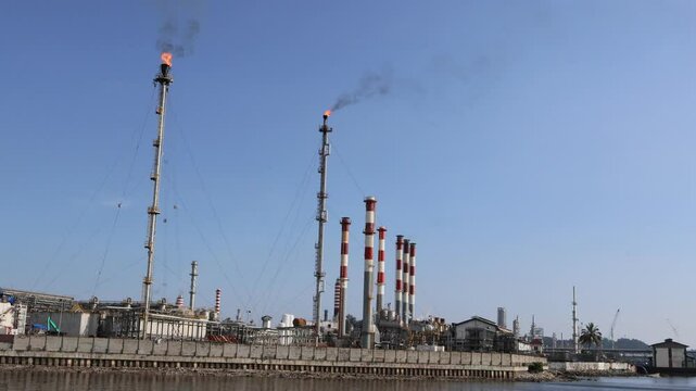 Balikpapan-East Kalimantan November 10,2024 A large pertamina oil refinery with storage tanks,high pipe,and smokestacks sits on the shore of a blue ocean
