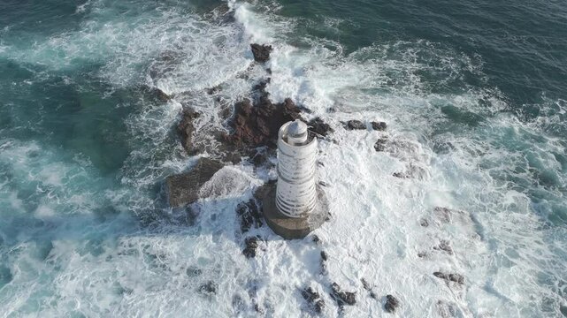 ripresa aerea di un faro in mezzo al mare su uno scoglio in Sardegna durante una forte mareggiata con onde forti che si infrangono sulle rocce