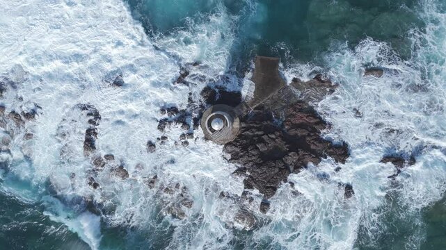 ripresa verticale cinematica aerea di un antico faro in uno scoglio in mezzo al mare durante una mareggiata 