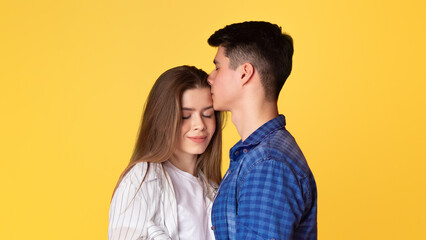 Young guy kisses lady in forehead isolated on yellow background