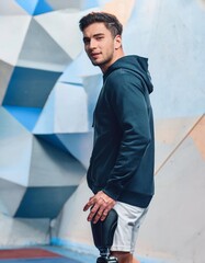 Athletic Young Man with a Hoodie and Prosthetic Leg Posing Against Blue Geometric Background