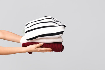 Female hands with stack of warm clothes on grey background