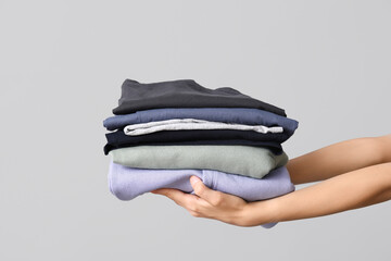 Female hands with stack of different clothes on grey background