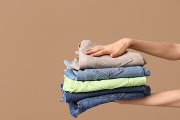Fototapeta premium Female hands with stack of different jeans on beige background