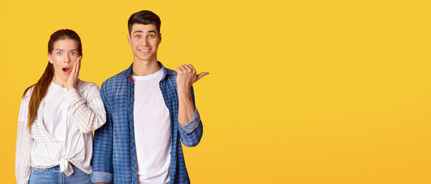 Gossip, tips and amazing information. Young beautiful lady with open mouth look at camera and shocked man, shows finger to free space, isolated on yellow background, studio shot, panorama, cut out