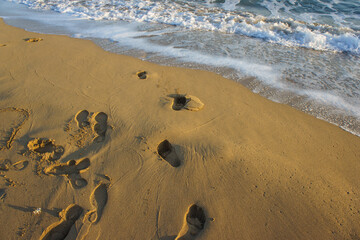 Footprints in wet sand at the shoreline during a tranquil sunset on a serene beach.