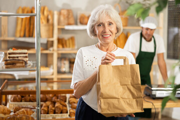 Elderly woman shopper with paper bag of fresh baked goods in bakery