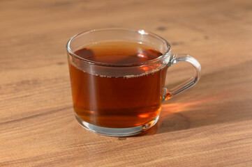 A cozy glass of freshly brewed tea resting on a wooden table in the warm afternoon sunlight