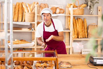 Polite middle-aged salesman holding a service clip while ready to assist customers in bakery