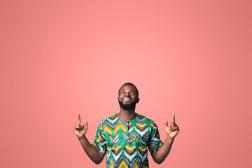 Happy black guy in african costume pointing up at free space, showing advertisement on blue studio background. Positive african american man looking up, directing at empty space for text