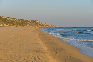 A serene beach at sunset with gentle waves and golden sands stretching towards the horizon.