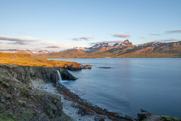 Naklejka premium Waterfall in Iceland feeding into the sea at sunrise with mountains in the background
