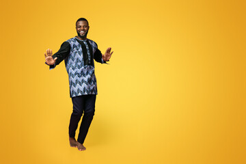 Bouncy african american guy in traditional costume dancing over pink studio background, full size photo. Funky young black man having fun, showing traditional moves. Africa concept