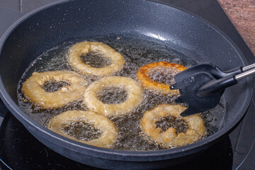 tongs removing fried and toasted battered squid rings from the pan