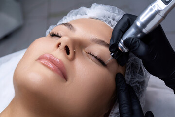 A beautician does permanent eyeliner makeup on a woman. Tattooing in a beauty salon.