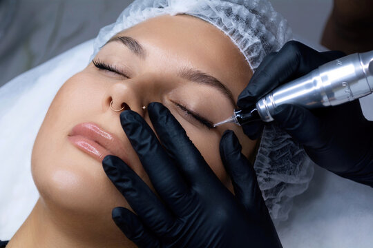 A beautician does permanent eyeliner makeup on a woman. Tattooing in a beauty salon.
