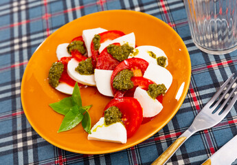 Caprese salad, sliced fresh mozzarella and tomatoes, served with basil leaves and pesto sauce.