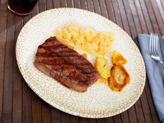 Grilled beef slice and some potatoes served with sauerkraut in a plate with other table appointments