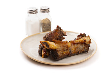 Two big juicy smoked meaty BBQ beef ribs on a plate with restaurant style salt and pepper shakers isolated on white