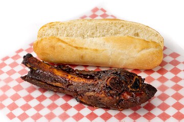 A big juicy smoked meaty BBQ beef rib and a cut open submarine bun on red paper isolated on white