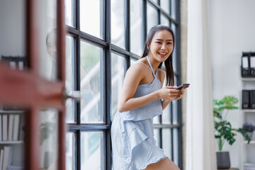 Cheerful beautiful Asian woman holding smartphone in the office workplace,
