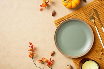 Autumn dining table setting with pumpkins, leaves, acorns, and cutlery on a beige background. Perfect for Thanksgiving, fall decorations, and seasonal food presentations