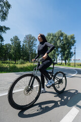 Fototapeta premium Caucasian woman riding a bike in a park. Vertical photo. 