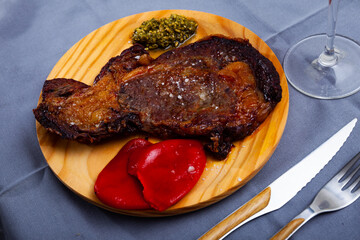 Delicious fried beef entrecote served with pesto sauce and marinated pepper on wooden board