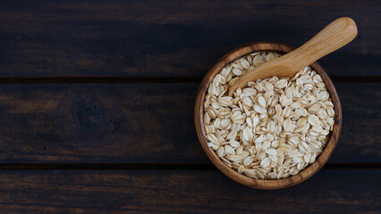 Wooden bowl filled with rolled oats on dark rustic table, ideal for healthy food concepts.