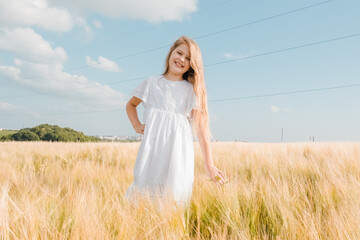 Little girl in a field with hay rolls at sunset.Profile side view little cute happy blond caucasian girl enjoy walking ripe wheat ear field.