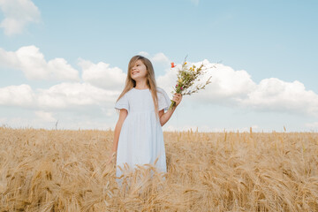 Beautiful summer girl in a field with rye. The girl holds a bouquet of cornflowers in her hands. Smiling girl with a bouquet of flowers in a rye field.