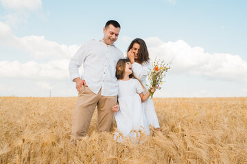 Happy family on a summer walk, mother, father and child walk in the wheat field and enjoy the beautiful nature, at sunset.